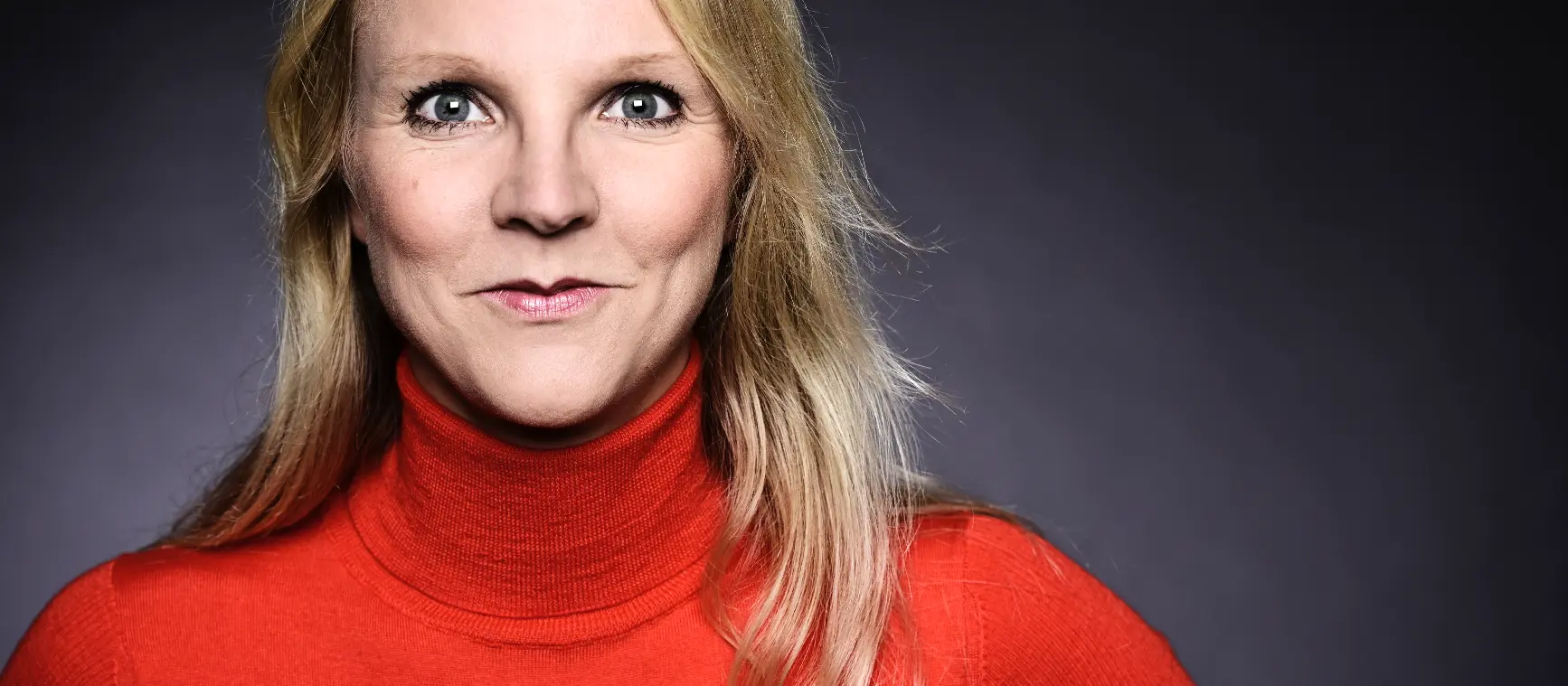 Janina Tiedemann in Nahaufnahme in rotem Pullover vor grauem Hintergrund.